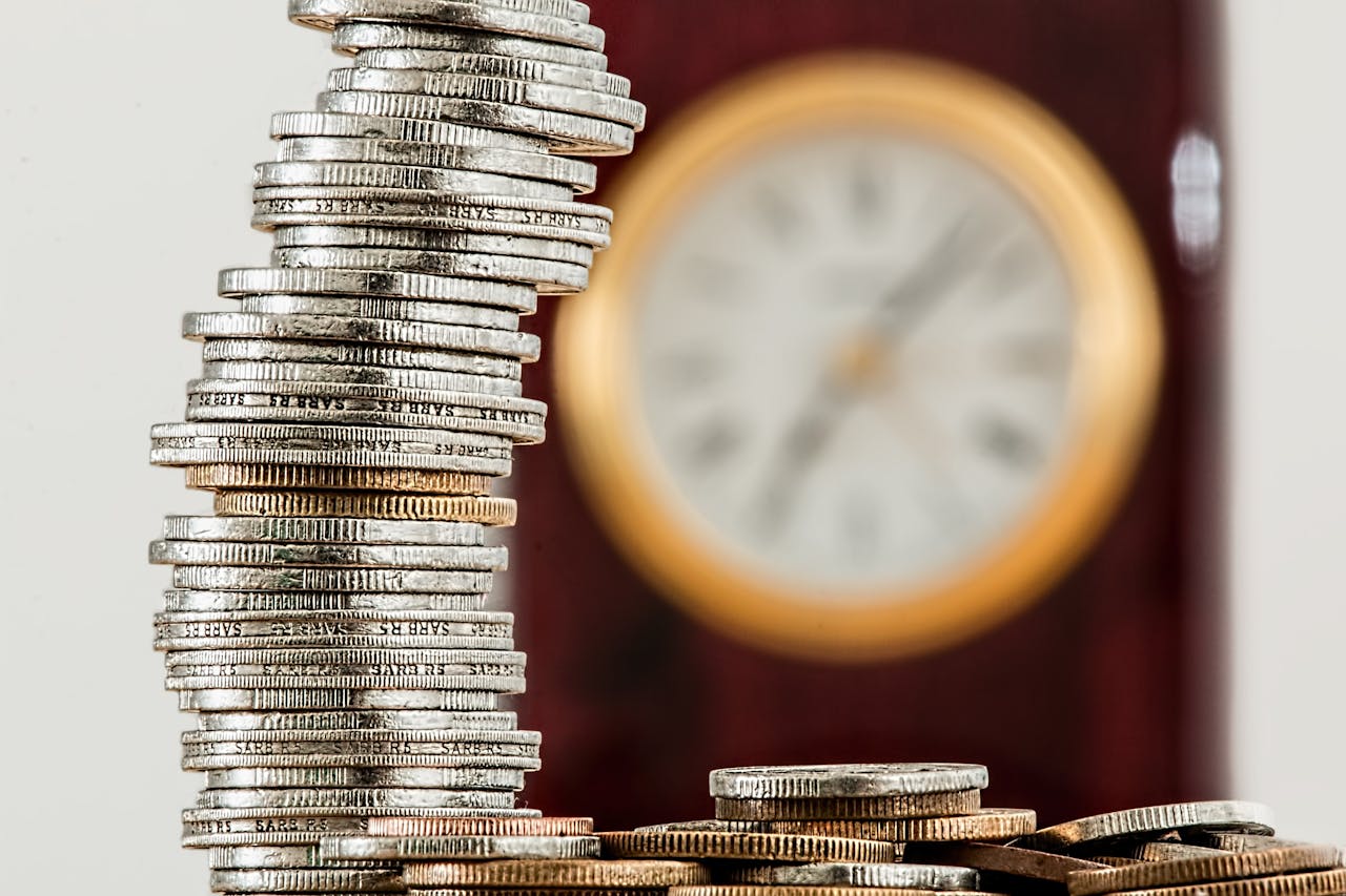 about-01 A close-up image of stacked coins with a blurred clock, symbolizing time and money relationship.